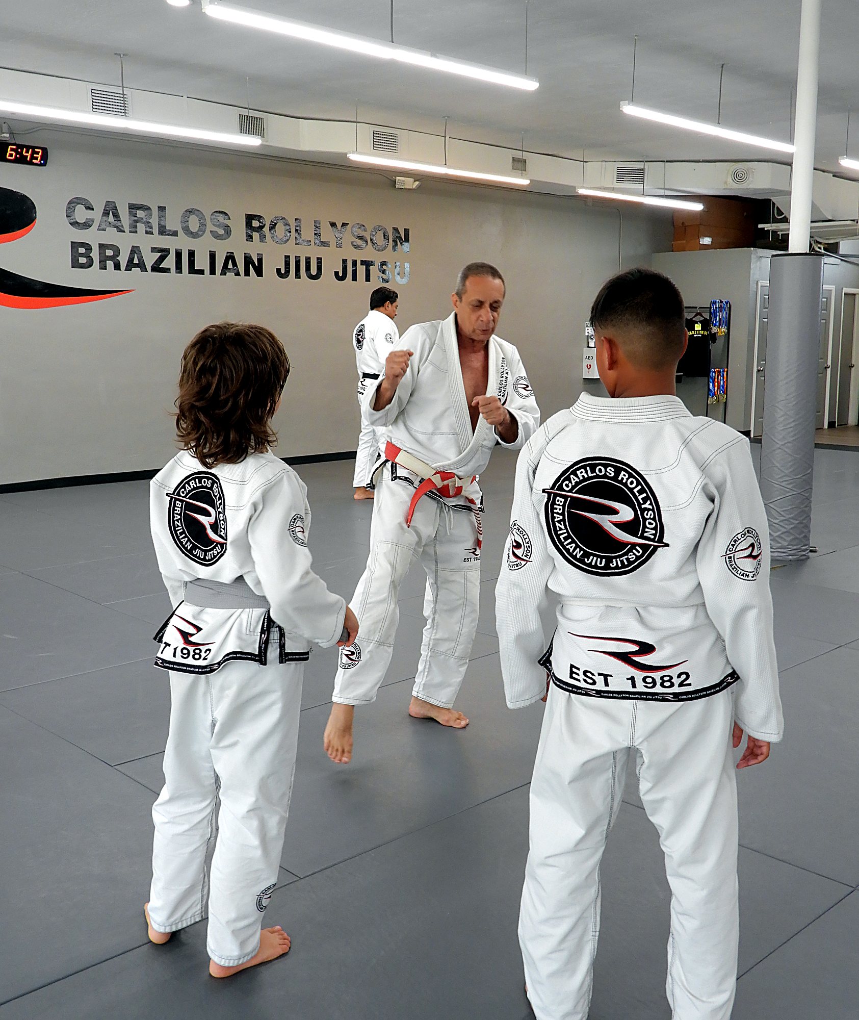 Master Carlos Rollyson coaching two kids in front of the Carlos Rollyson logo wall